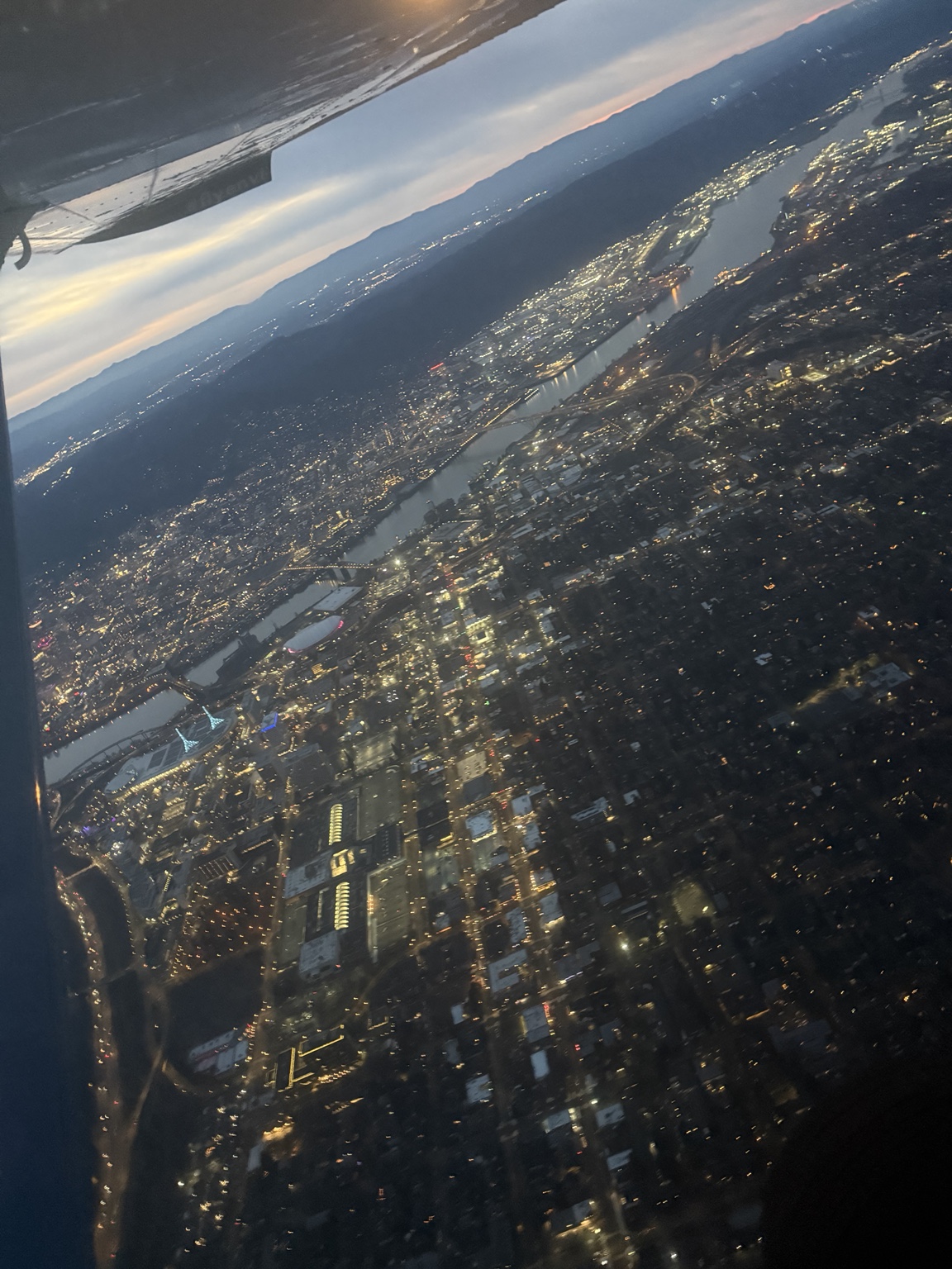 A tilted view of Portland city lights and the Willamette River beneath an airplane wing